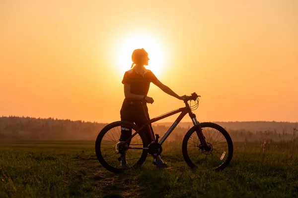 Happy girl with a bicycle on the nature on the background of bright sunset and yellow sun