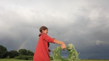 Ulusal elbiseyle bir kadın, fırtınlı bir gökyüzünün arka planında çiçek çelenk ile dönüyor. Yavaş hareket