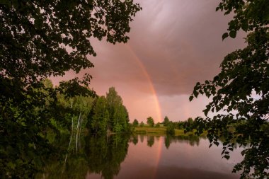 Bir orman gölet yansıması ile gökkuşağı ve kırmızı-sarı gün batımı.