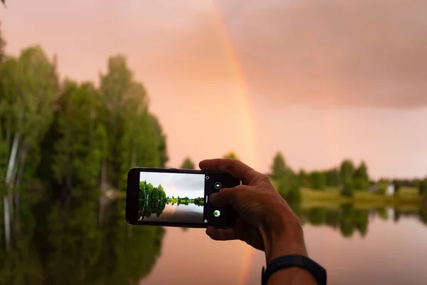 Photographing a landscape on a smartphone. Rainbow and red-yellow sunset with reflection in a forest pond.