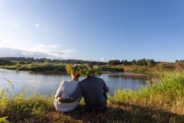 Birkaç genç, başlarının üzerinde çelenk le nehir kıyısında oturuyorlar. Çerçeveiçinde sunbeam