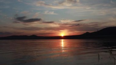 Bir dağ gölünde güzel yaz gün batımı. Dağlarda kırmızı güneş battı. Dalgalar kıyıya koşuyor