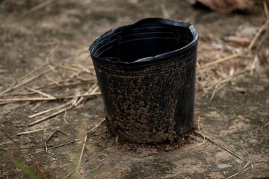 Bir sezonun sonunu ya da bir bahçe projesini temsil eden boş, kirli, siyah plastik bir tencerenin kurak zeminde oturduğu yakın plan bir hayat..