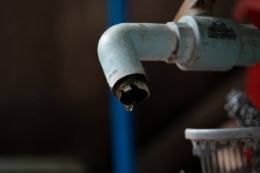 Eski, kirli ve çürümüş bir musluktan dökülen tek bir damla suyun güçlü makro görüntüsü, kırsal bir ortamda su kıtlığını, israfı veya yoksulluğu simgeliyor..