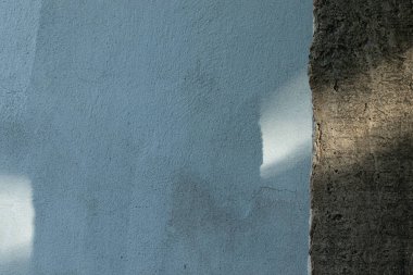 Pürüzsüz, ham beton bir kenarın yanında açık mavi boyalı bir duvar, parlak güneş ışığından küçük kıymıklar ve ilginç gölgeler oluşturan ve gölgeler yaratan minimalist bir mimari arka plan..