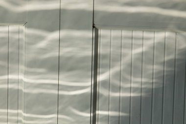 Yakıcı ışık desenlerinin soyut arkaplanı, sudan yansıyan güneş ışığı beyaz panelli bir yüzey üzerinde büyüleyici dalga dalgaları yaratıyor.