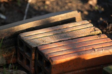 Bir yığın eski, kirli kırmızı tuğla sıcak güneş ışığında yerde yatıyor. İnşaat ve inşaat malzemelerinin kırsal bir zemin oluşturuyor.