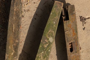 An abstract top-down composition of three old, weathered wooden posts on the ground, with strong diagonal lines and shadows from the sun
