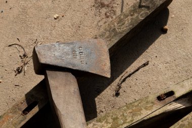 Close-up of an old, rustic axe tool lying on wooden planks under harsh sunlight, creating a strong shadow on a sandy background