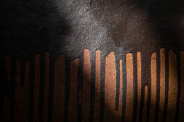 Güçlü çapraz ışık altında koyu bir yüzeye bakır veya kahverengi boya damlayan dramatik ve karamsar bir soyut doku.