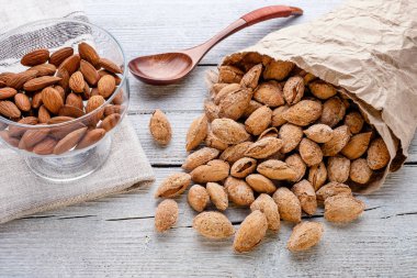 Beyaz ahşap arka plan, keten peçete ve tahta kaşık kağıt torba içinde deniz hayvanı kabuğu içinde tuzlu badem