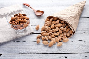 Beyaz ahşap arka plan, keten peçete ve tahta kaşık kağıt torba içinde deniz hayvanı kabuğu içinde tuzlu badem