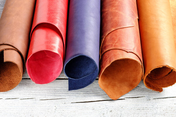 Brightly colored leather in rolls on the white wooden background. Leather craft.