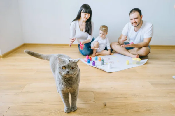 little boy  with parents and a cat painting a poster and one another with paints