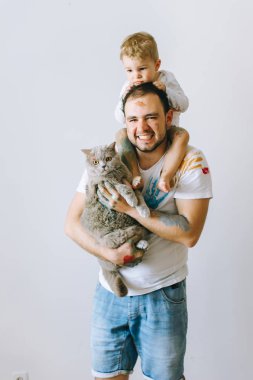 Baba ile oğlu onun omuzlarında ve elindeki boya ile boyanmış bir kedi