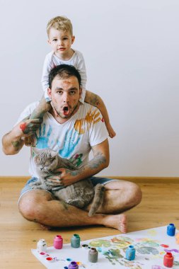 Baba ile oğlu onun omuzlarında ve elindeki boya ile boyanmış bir kedi