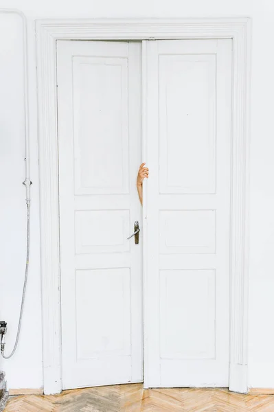 woman\'s hand opens a white door to a white room with a lacquered parquet