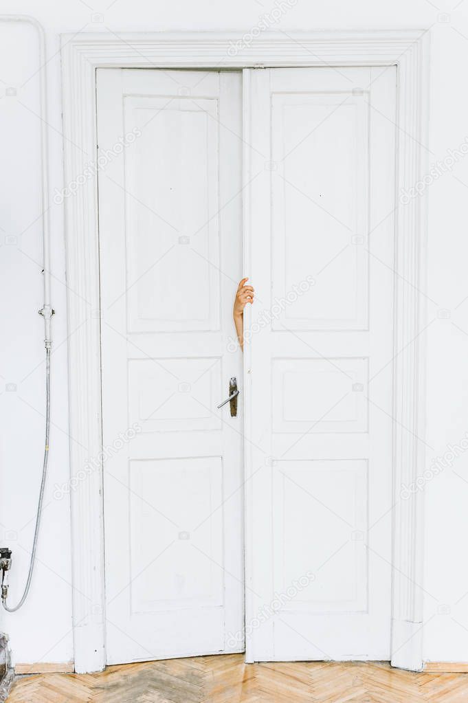 woman's hand opens a white door to a white room with a lacquered parquet
