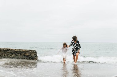 Anne ve kızı elele ve sahilde yürüyüş