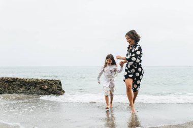 Anne ve kızı elele ve sahilde yürüyüş