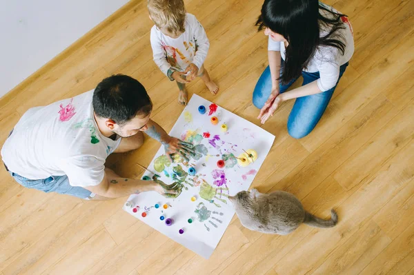 son with parents and a cat painting a poster and one another with paints