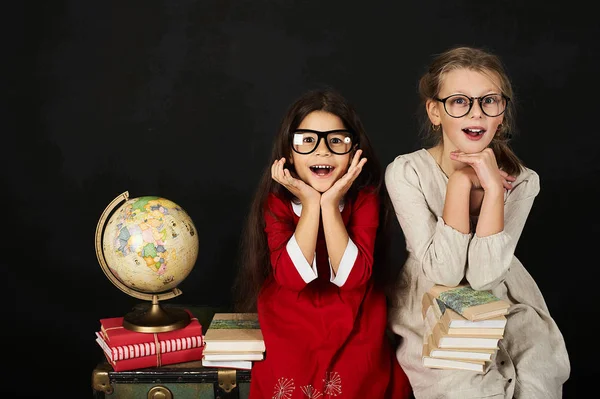 two happy schoolgirls with globe and books sitting on chest on a black background