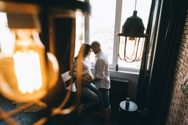 Gebelik ve insanlar kavramı - pencerede evde duran hamile eşi ile mutlu bir adam