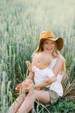Genç bir anne ve buğday yeşil bir arka plan üzerinde oturan küçük çocuk