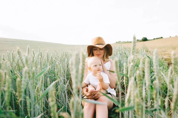 若い母親と小さな子供緑の背景に小麦のそばに座って — ストック写真