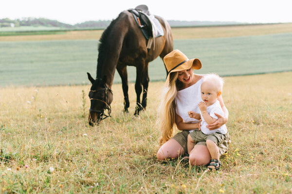 young woman and baby boy have a fun in the field. Parent and child with a horse in the field 