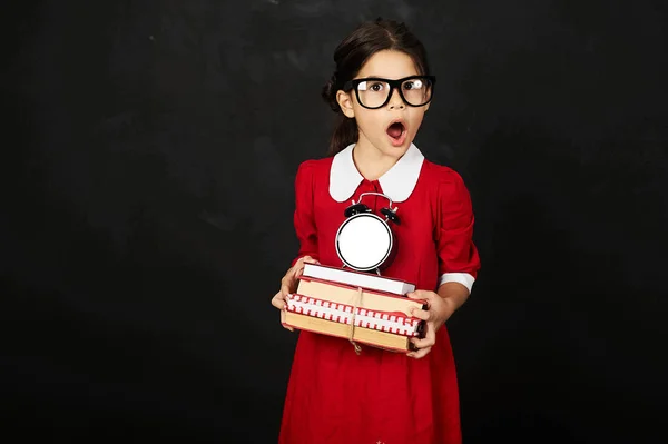 schoolgirl in a red dress with a books and clock on a black background