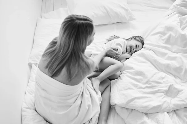 Una hermosa madre embarazada y su hija jugando en una cama blanca en — Foto de Stock