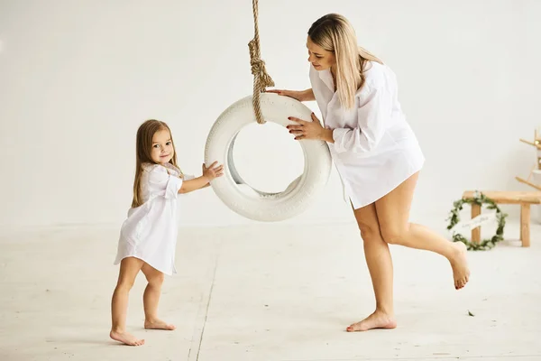 A beautiful pregnant mom plays with her daughter on a swing in a — Stock Photo, Image