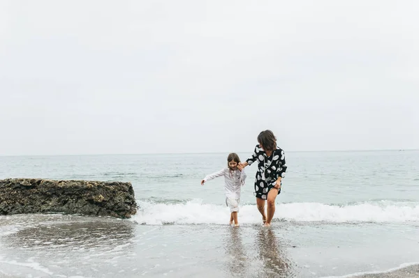 Мать и дочь держатся за руки и ходят по пляжу. Мама и... — стоковое фото