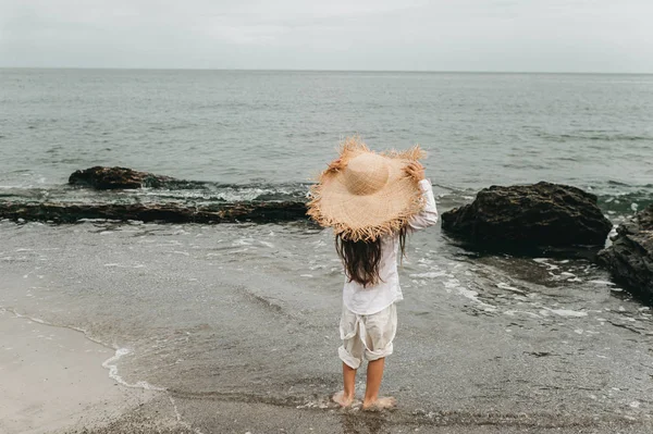 Adorable niña en sombrero de paja en la playa durante las vacaciones de verano —  Fotos de Stock