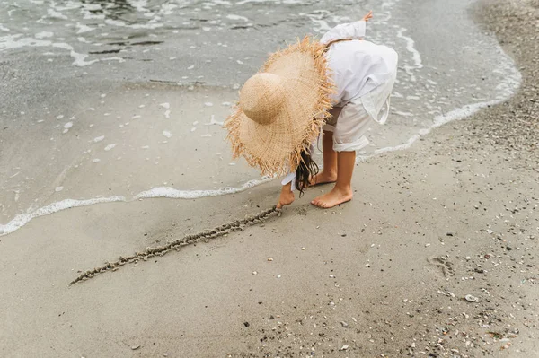 Adorable niña en sombrero de paja en la playa durante las vacaciones de verano — Foto de Stock