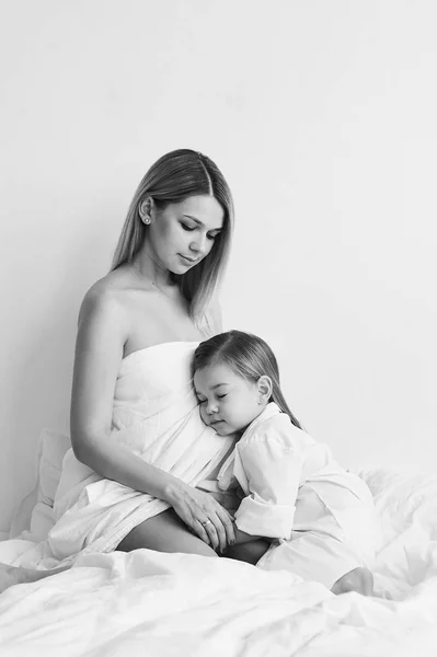Eine schöne schwangere Mutter und Tochter spielen auf einem weißen Bett in — Stockfoto