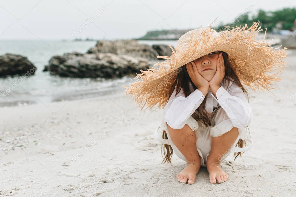 Adorable little girl in straw hat at beach during summer vacatio