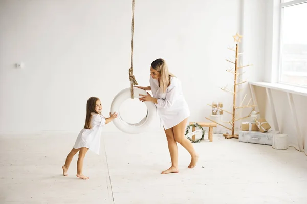 Een mooie zwangere moeder speelt met haar dochter op een schommel in een — Stockfoto