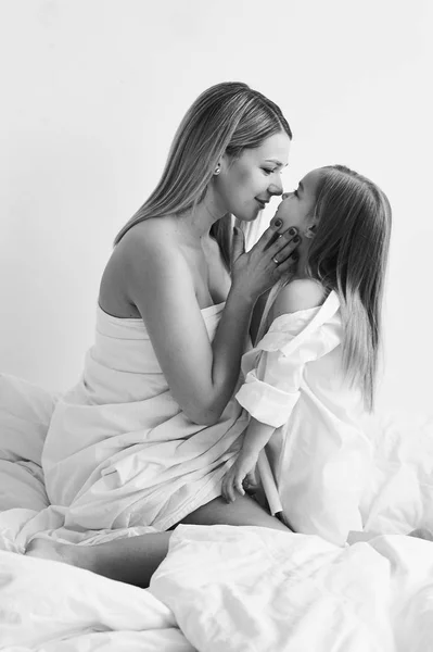Красивые беременные мама и дочь играют на белой кровати в — стоковое фото