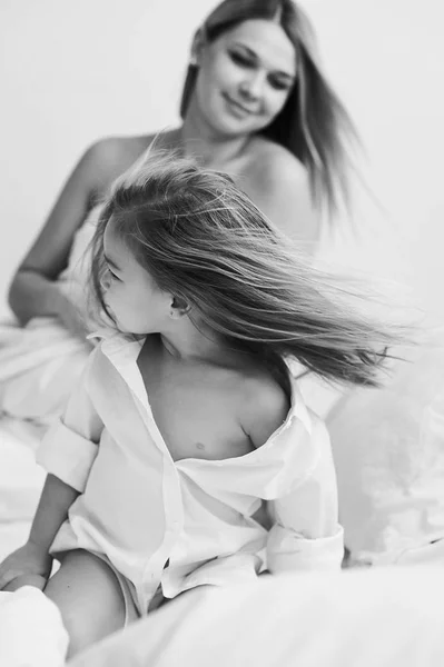 Uma bela mãe grávida e filha brincando em uma cama branca em — Fotografia de Stock