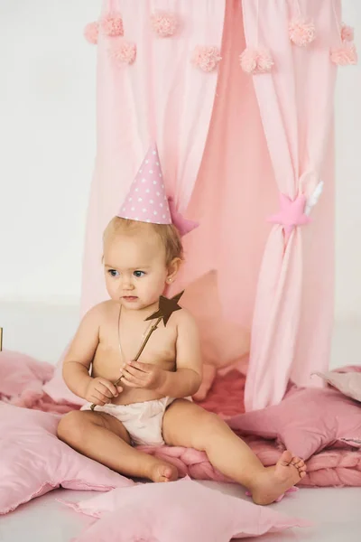 Een kleine baby in een roze tent met een toverstaf in de buurt van een grote taart. — Stockfoto