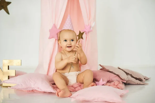 Een kleine baby in een roze tent met een toverstaf in de buurt van een grote taart. — Stockfoto