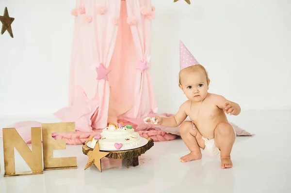 Een kleine baby in een roze tent met een toverstaf in de buurt van een grote taart. — Stockfoto