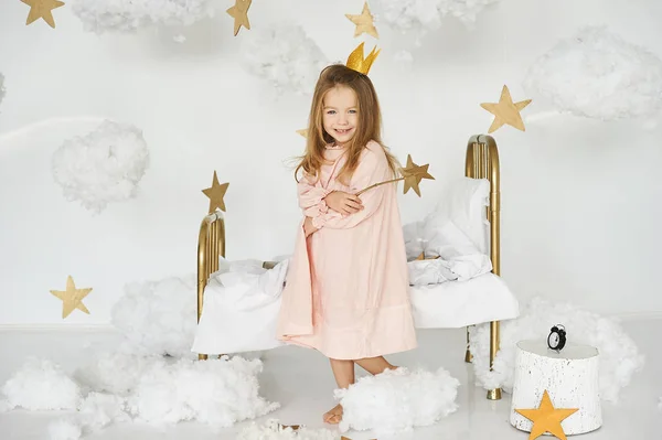 Malá princezna s kouzelnou hůlkou na posteli v oblacích — Stock fotografie