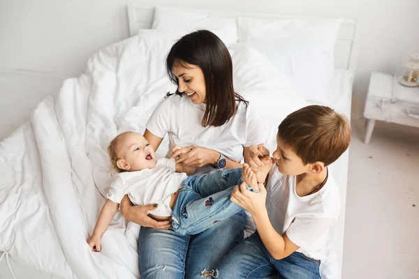 Glad kärleksfull familj. Mamma leker med hennes barn i sängen — Stockfoto