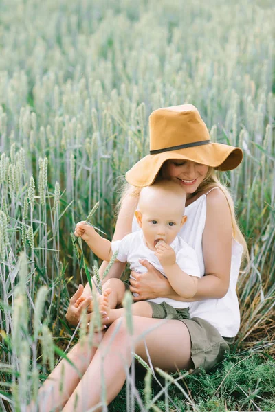 Молодая мать и ее маленький ребенок, сидящие рядом с пшеницей на — стоковое фото