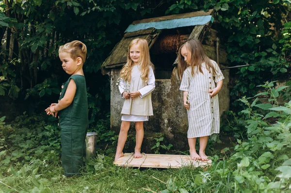 Tre bambini stanno giocando vicino al pozzo su uno sfondo di gras — Foto Stock