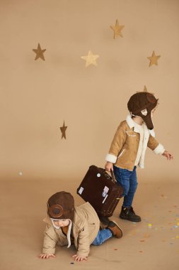 İki kardeş bir oyuncak uçak ve bir bavul bej renkli arka plan üzerinde oynanır. rüyalar ve seyahat kavramı