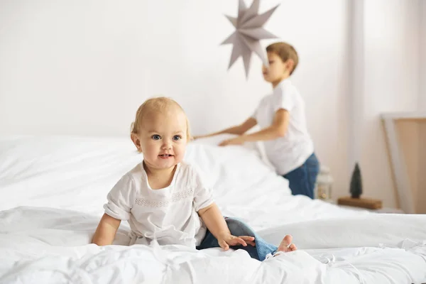 白い寝室で遊んで幸せな子供たち 男の子と女の子 弟と妹をベッドの上プレイします — ストック写真